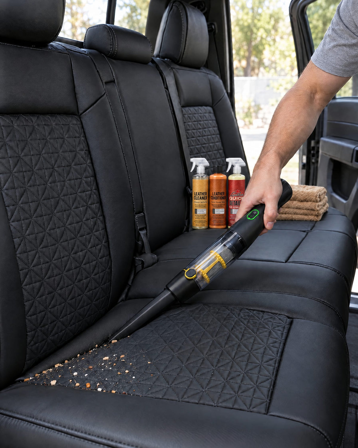 Cordless handheld vacuum cleaning crumbs from a black leather seat cover